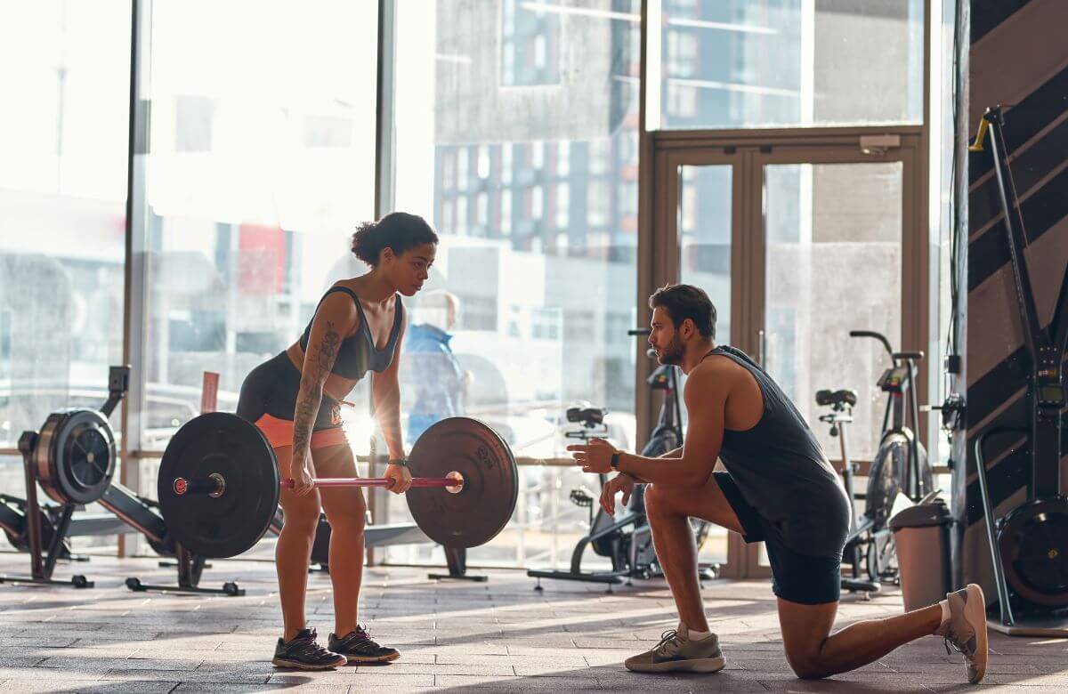 Woman being coached on how to perform Romanian deadlifts with perfect form as part of a workout routine.