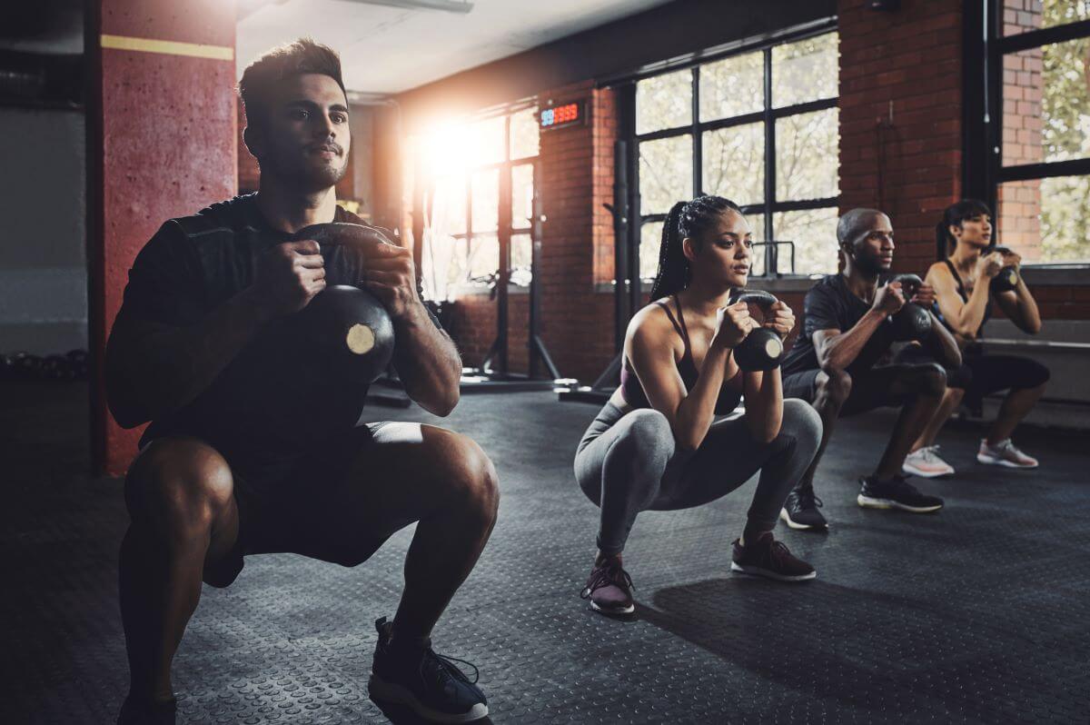 Fitness group performing a kettlebell squat during a 3 day kettlebell workout routine