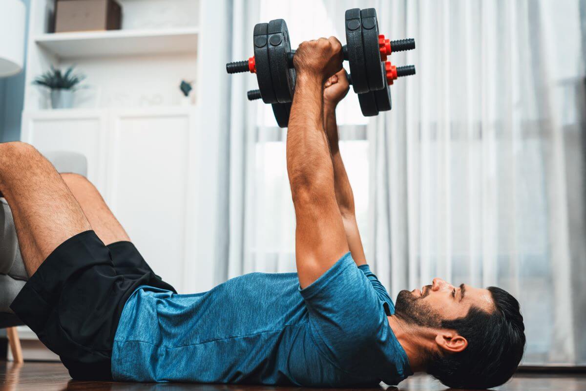 Man performing dumbbell floor press exercise in 3 day total body dumbbell workout