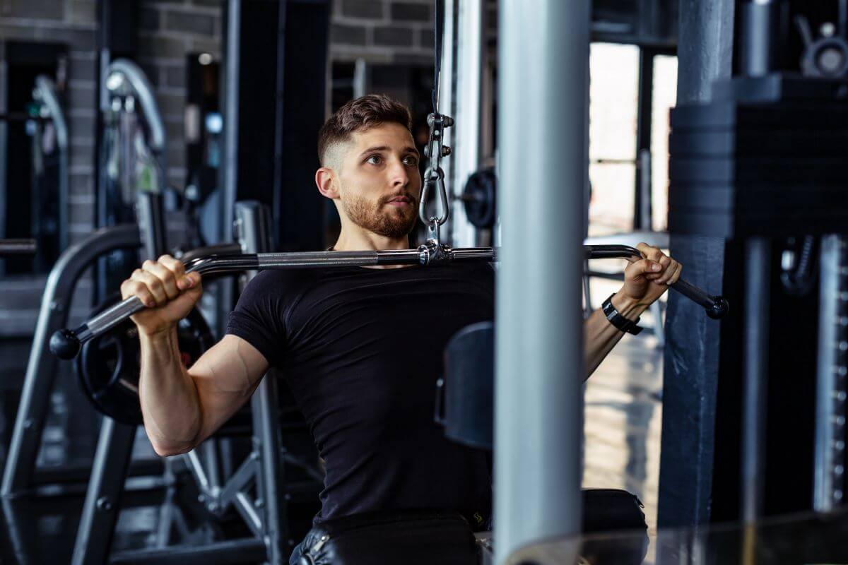 Man performing lat pull downs as part of a 4 day planet fitness upper/lower workout routine