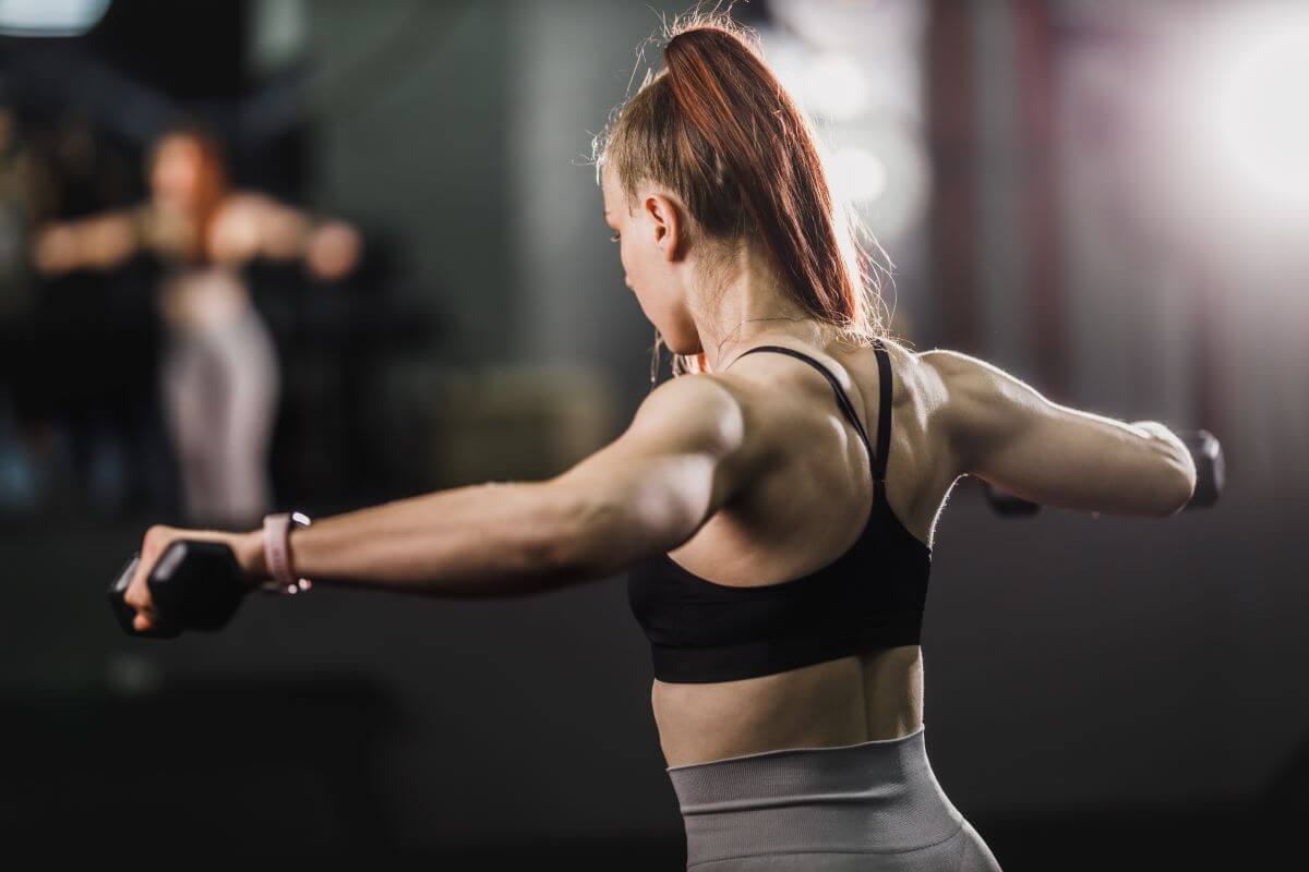 Woman performing dumbbell shoulder raises as part of dumbbell only shoulder workout